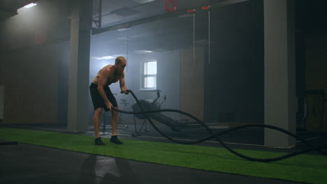 Fitness-man-exercising-with-battle-rope-abandoned-warehouse.-Tough-man-working-out-in-cross-training-gym-made-inside-old-factory.